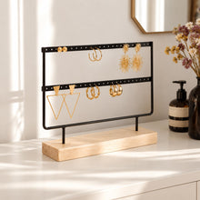 Charger l'image dans la galerie, Présentoir à boucles d'oreilles noir et bois avec créoles et boucles pendantes dorées, posé sur une commode blanche