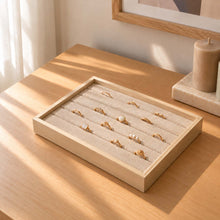 Charger l'image dans la galerie, Plateau à bagues en bois et tissu beige garni de bagues dorées, posé sur une commode
