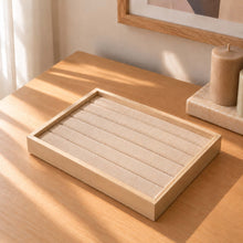 Charger l'image dans la galerie, Plateau à bagues vide en bois clair et tissu beige sur une commode en bois, près d'une fenêtre
