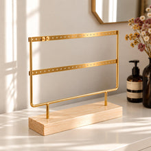 Charger l'image dans la galerie, Porte-boucles d'oreilles doré à deux rangées avec socle en bois naturel, présenté sur une commode blanche
