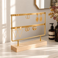 Charger l'image dans la galerie, Présentoir à boucles d'oreilles doré avec créoles et boucles pendantes, posé sur une commode blanche
