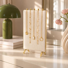 Charger l'image dans la galerie, Présentoir à colliers en velours écru avec cinq colliers dorés, posé sur une commode blanche

